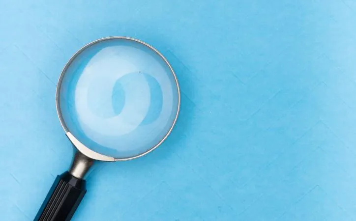 Picture of a magnifying glass with a black handle in front of a light blue background