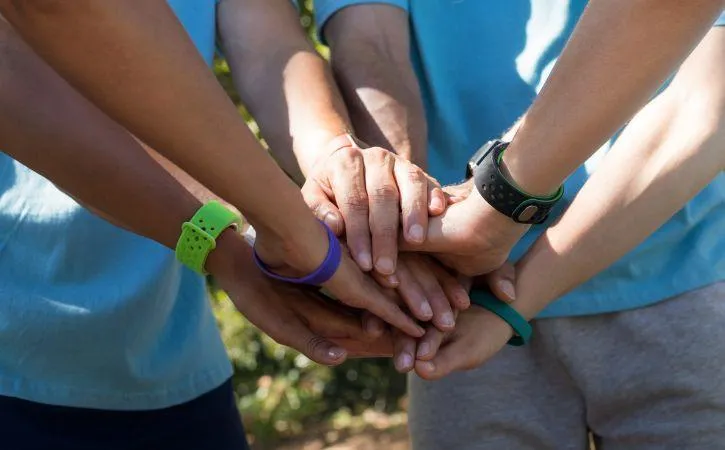 picture shows 5 young people's hands on top of each other. They are wearing colourful watches and bracelets.