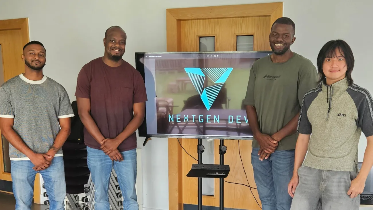 Four smiling men in casual clothes are standing next to a television screen that says Next Gen Dev in capital letters, and the NextGen Dev logo
