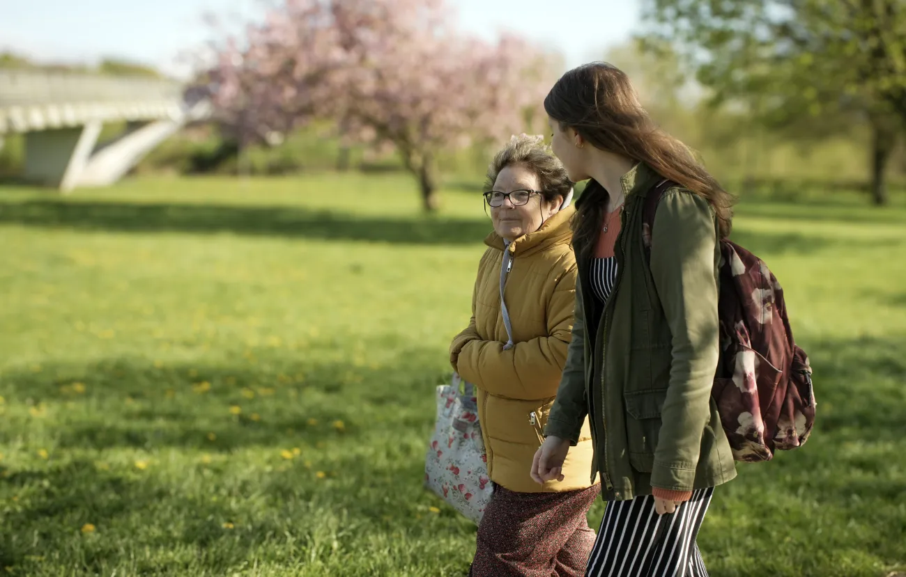 Two women walk in a beautiful sunny field with a blossom tree in the background