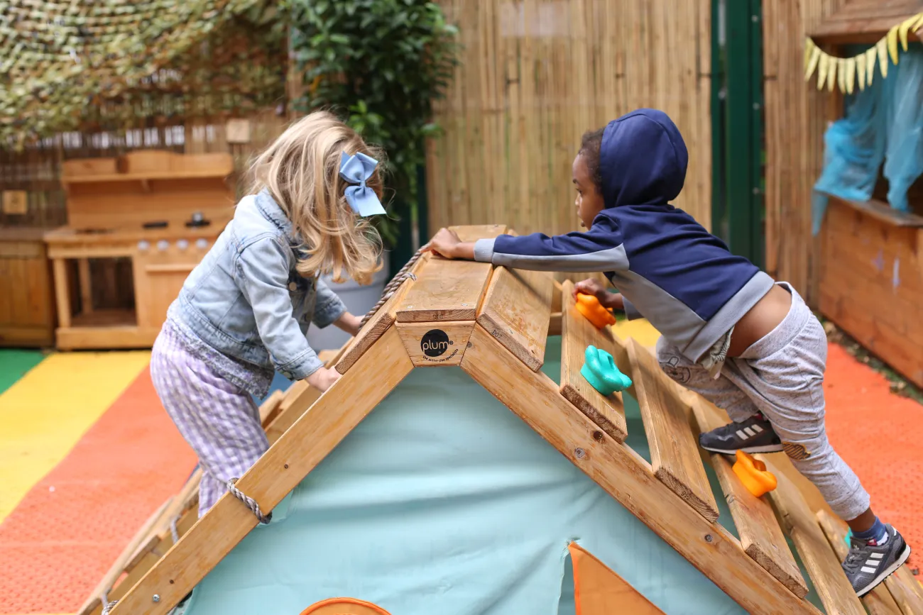 Two young children playing on a low wooden climbing wall. 