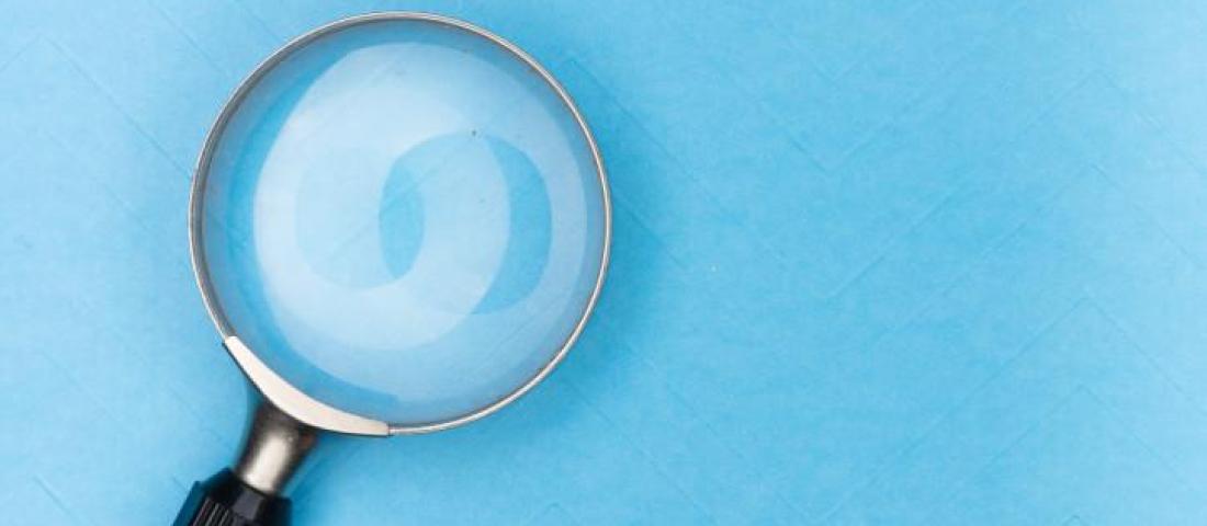 Picture of a magnifying glass with a black handle in front of a light blue background