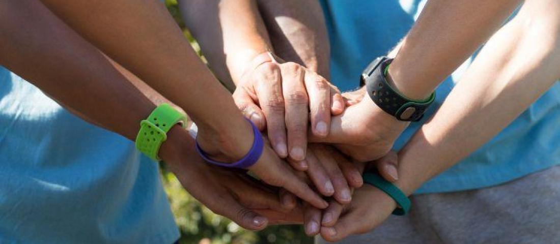 picture shows 5 young people's hands on top of each other. They are wearing colourful watches and bracelets.