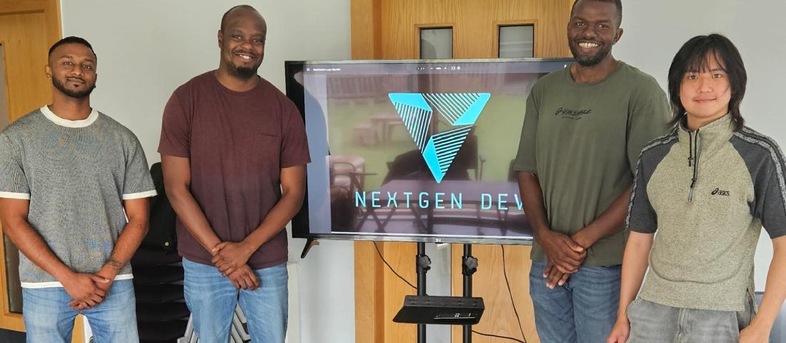 Four smiling men in casual clothes are standing next to a television screen that says Next Gen Dev in capital letters, and the NextGen Dev logo